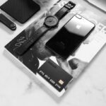 Black and white flat lay showcasing a stylish desk with phone, watch, and accessories.